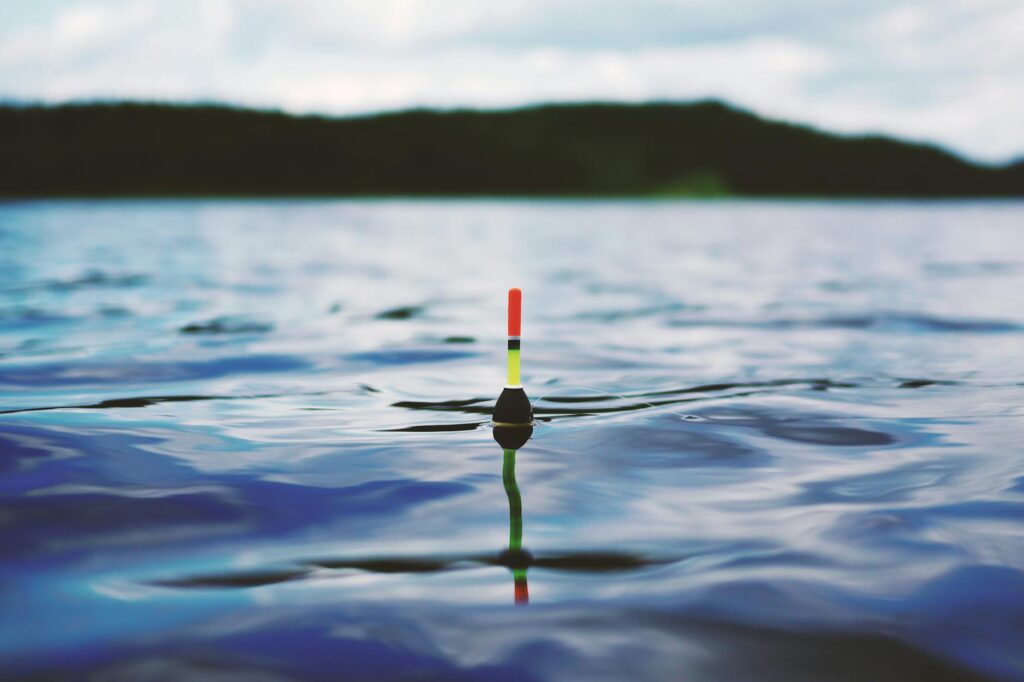 Vibrant fishing float gently resting on a serene blue water surface, ideal for travel and nature themes.