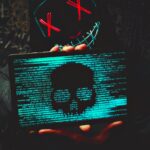 A mysterious person in a neon mask holds a tablet displaying a digital skull.