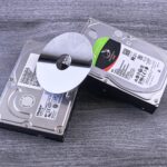 Two computer hard drives and a shiny disk displayed on a wooden surface.