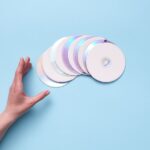 A hand reaching out to a stack of CDs on a blue backdrop, evoking nostalgia for retro technology.