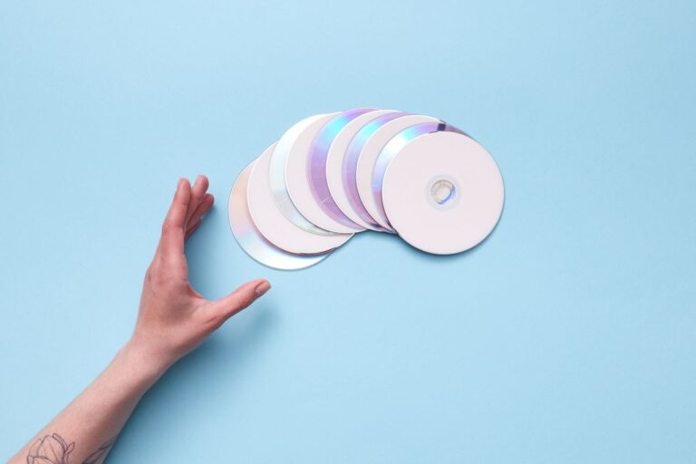 A hand reaching out to a stack of CDs on a blue backdrop, evoking nostalgia for retro technology.