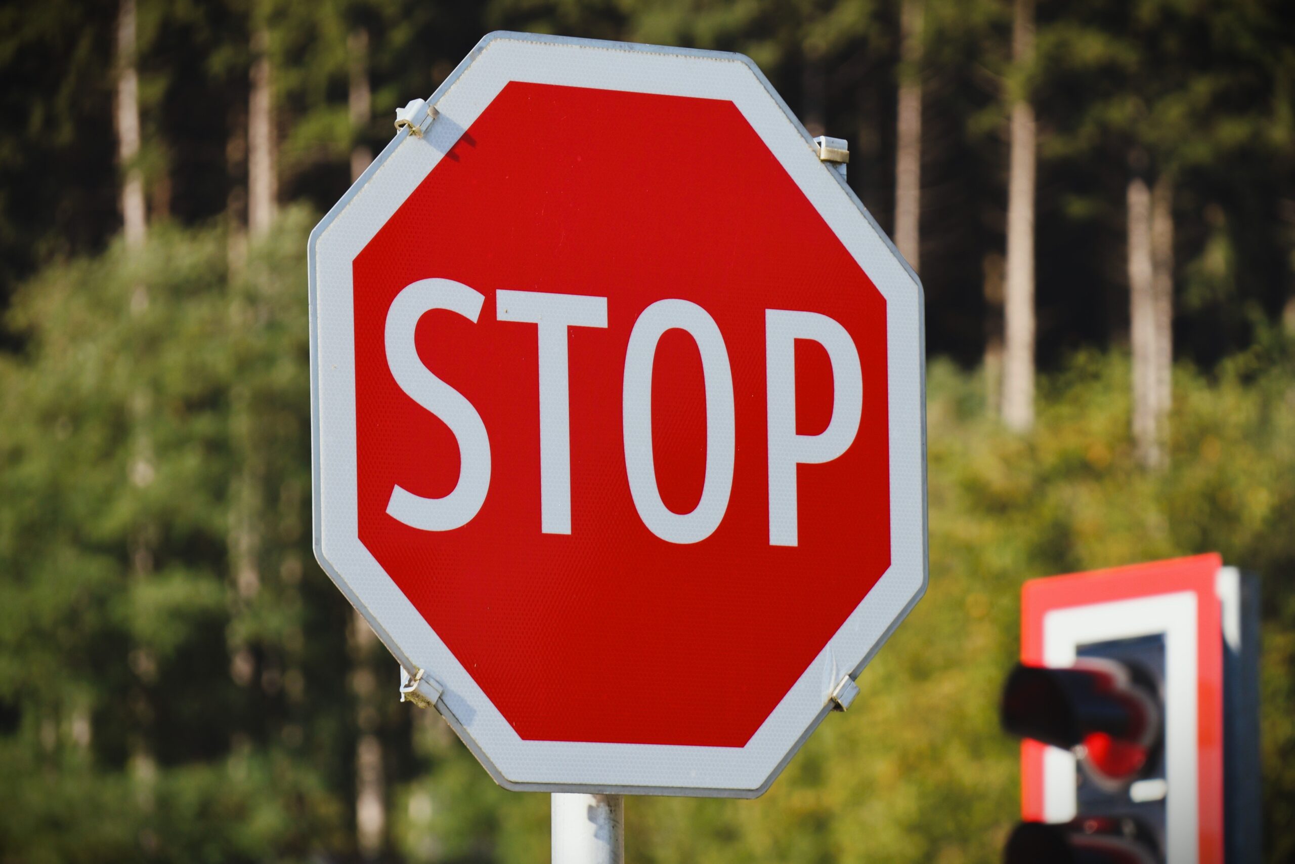 Close-up of a bright red stop sign against a background of lush green trees.