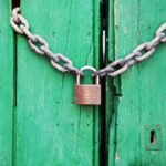 A rustic green wooden door secured with a heavy chain and padlock, symbolizing security.