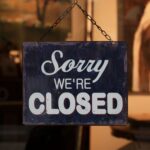 A 'Sorry We're Closed' sign hangs in a shop window, indicating closure.