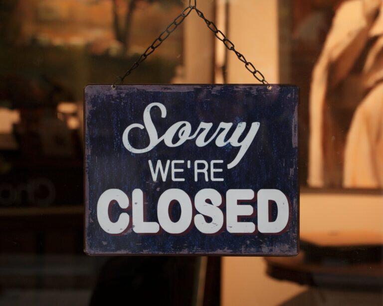 A 'Sorry We're Closed' sign hangs in a shop window, indicating closure.