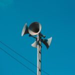 A set of loudspeakers on a pole against a bright blue sky, symbolizing communication and technology.