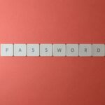 Focus on password security with white keyboard tiles spelling 'PASSWORD' on a coral background.