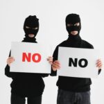 Two masked individuals holding "No" signs against a white background, concept of refusal or anonymity.