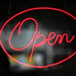 Close-up of a bright red neon 'Open' sign against a dark background.