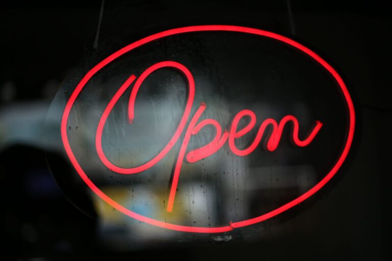 Close-up of a bright red neon 'Open' sign against a dark background.